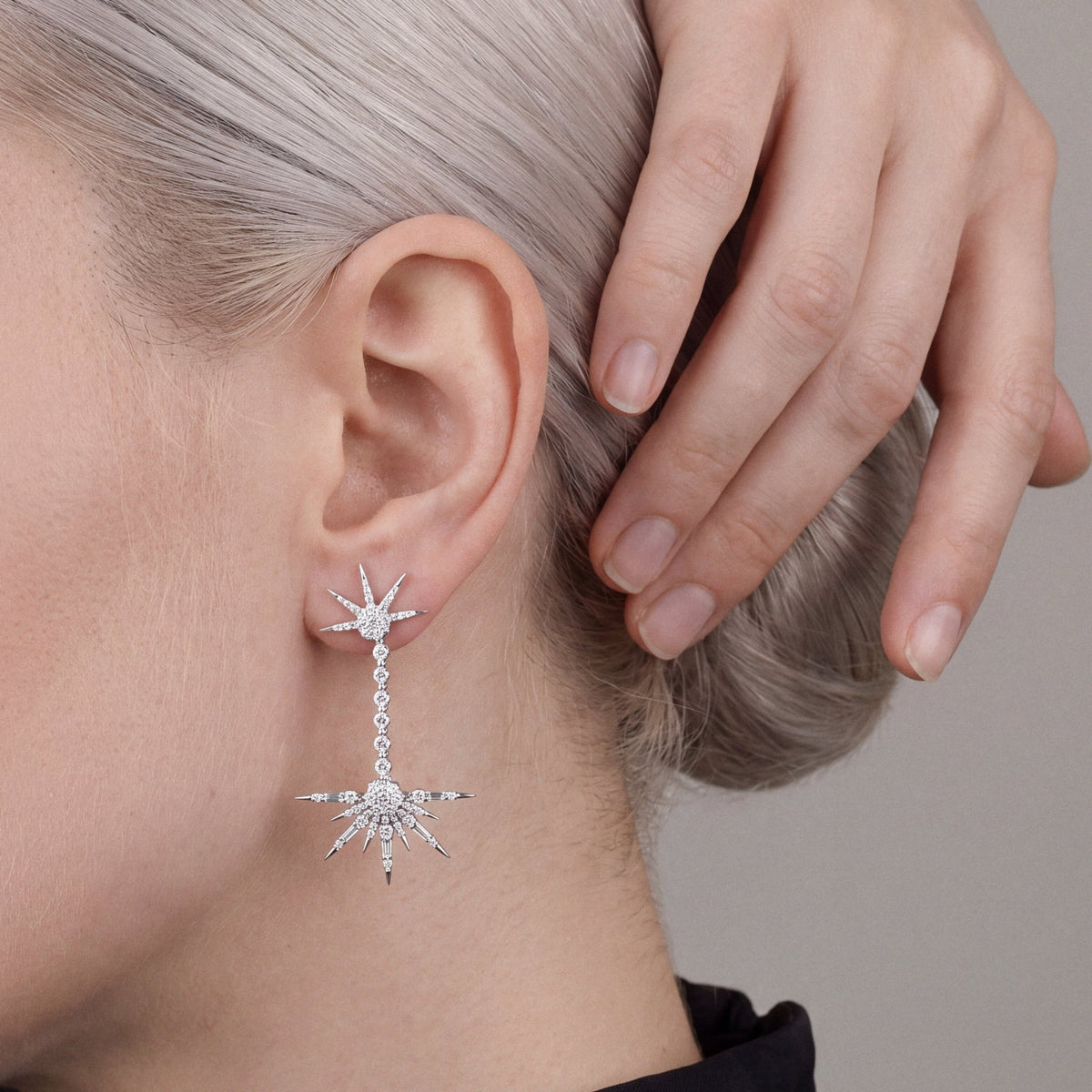 Woman in a black mock-neck top with her hand in her hair, wearing a natural diamond starburst drop earring in 18K white gold