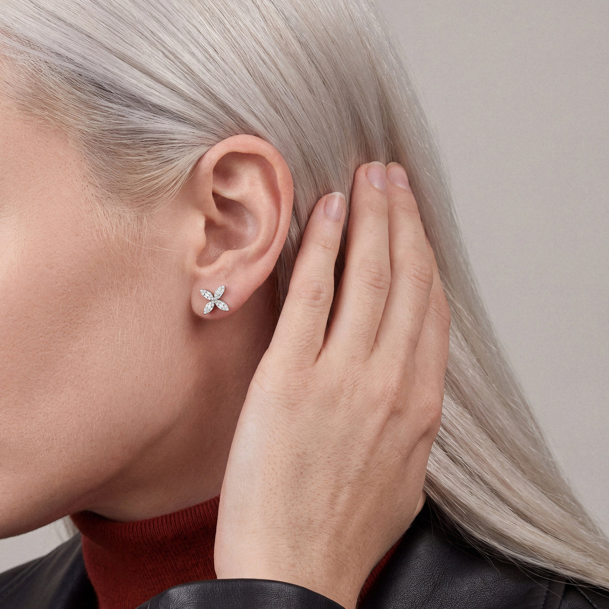 Woman in a black leather jacket pushing her hair behind her ear to show a baguette natural diamond flower stud earring in 14K white gold