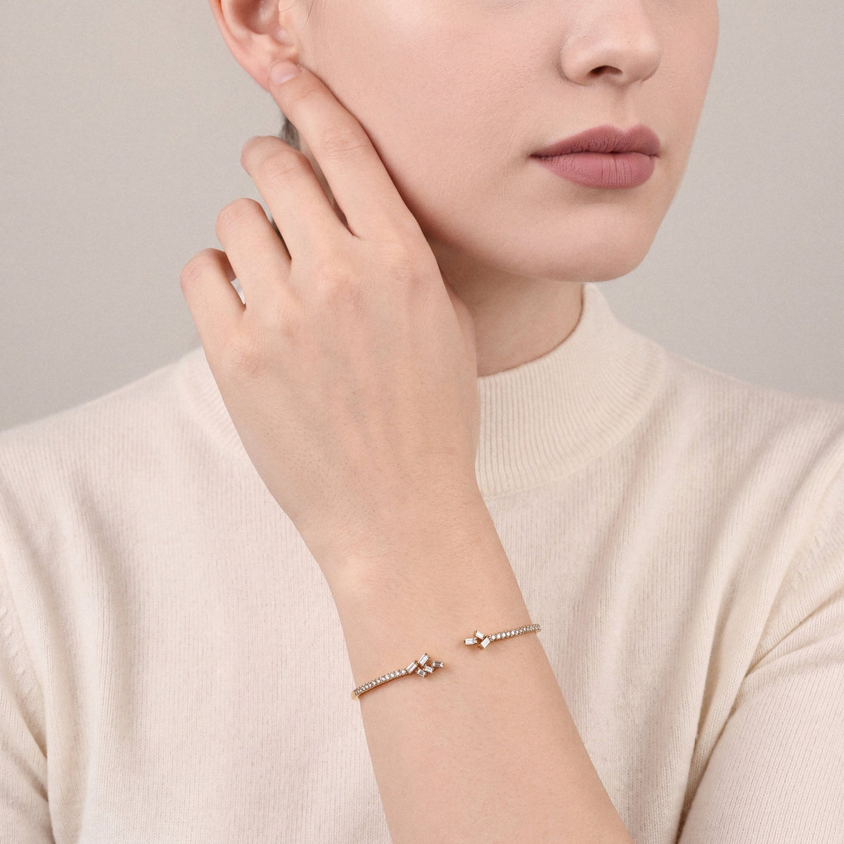 Woman in an ivory knit wearing a natural diamond baguette cluster open cuff bracelet in 18K yellow gold