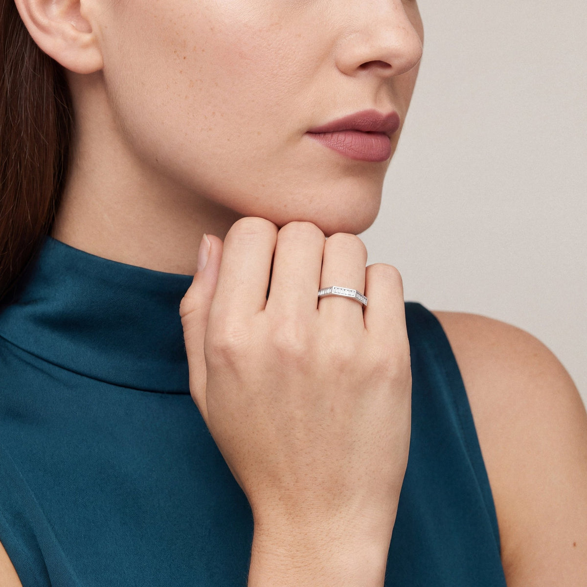 Woman in a teal satin high-neck top wearing a baguette diamond eternity ring in 14K white gold, hand at the chin