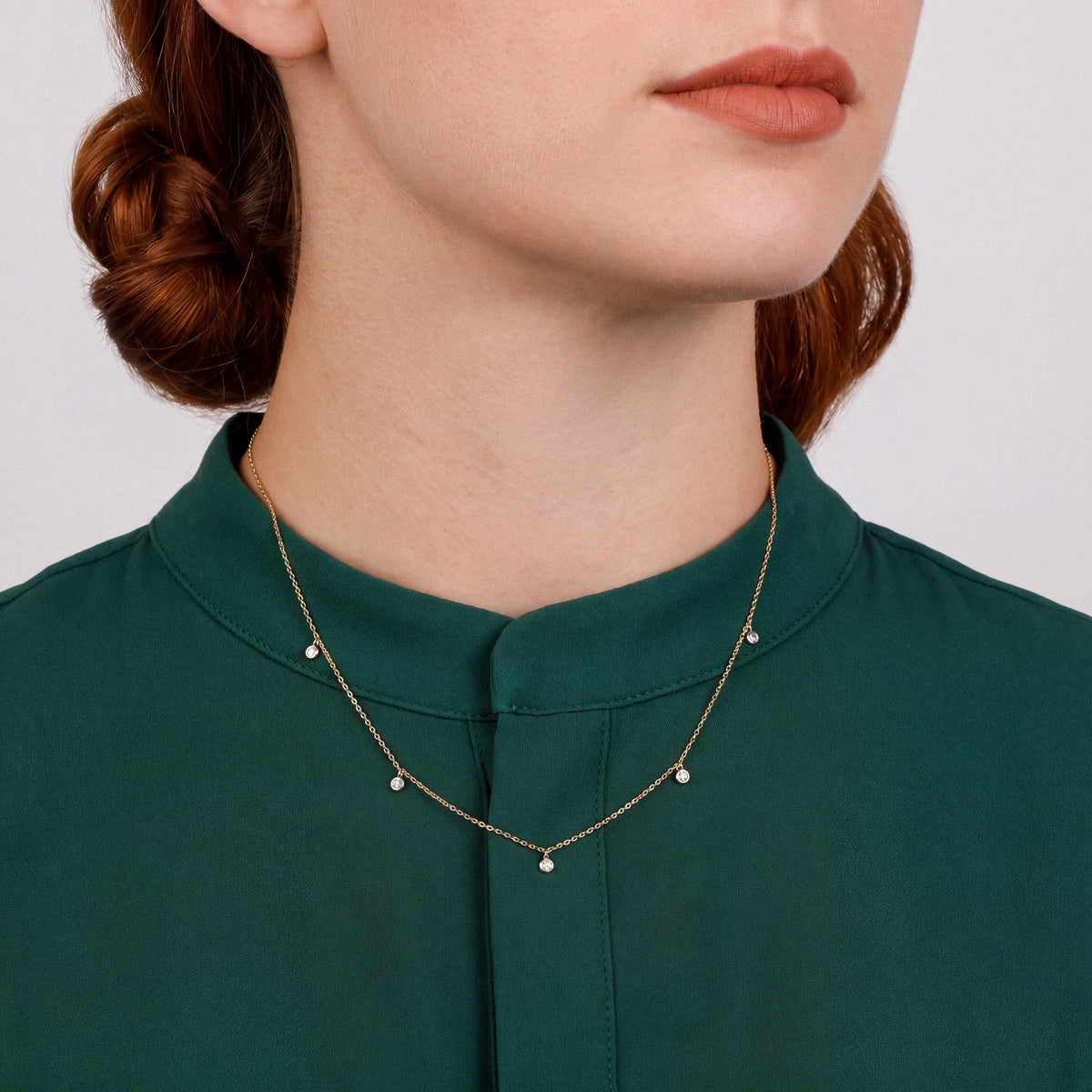 Woman in an emerald stand-collar blouse wearing a natural diamond bezel drop station necklace in 14K yellow and white gold