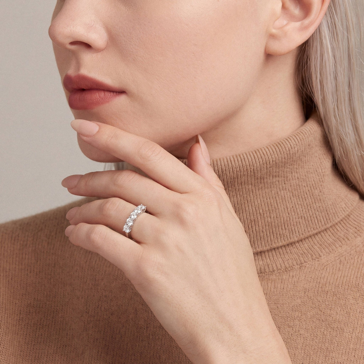 1.16 ct natural diamond five-stone ring in 14K white gold worn on the ring finger, fingertips at the chin, camel cashmere turtleneck