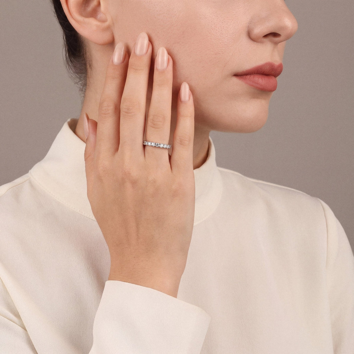 Model in an ivory silk high-neck blouse wearing a natural diamond full eternity ring in 14K white gold, hand on her cheek