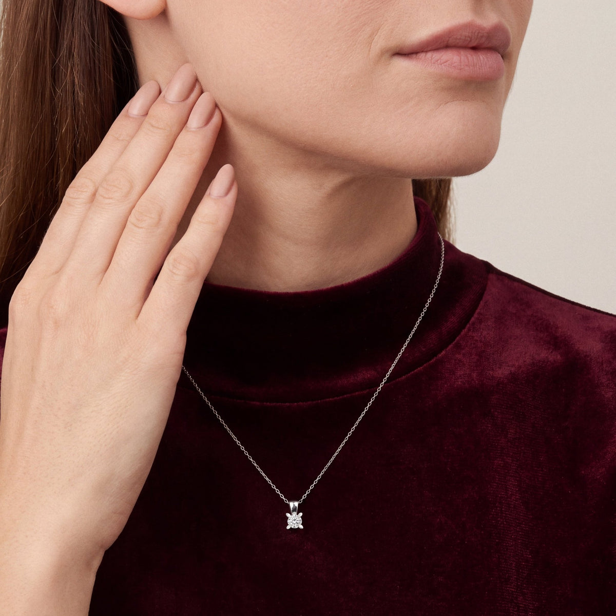 Woman in a burgundy velvet mock-neck top wearing a 0.50 ct natural diamond solitaire pendant necklace in 14K white gold