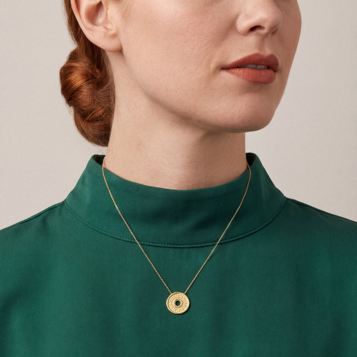 Woman in an emerald silk-crepe funnel-neck top wearing a natural diamond coin disc pendant necklace in 18K yellow gold