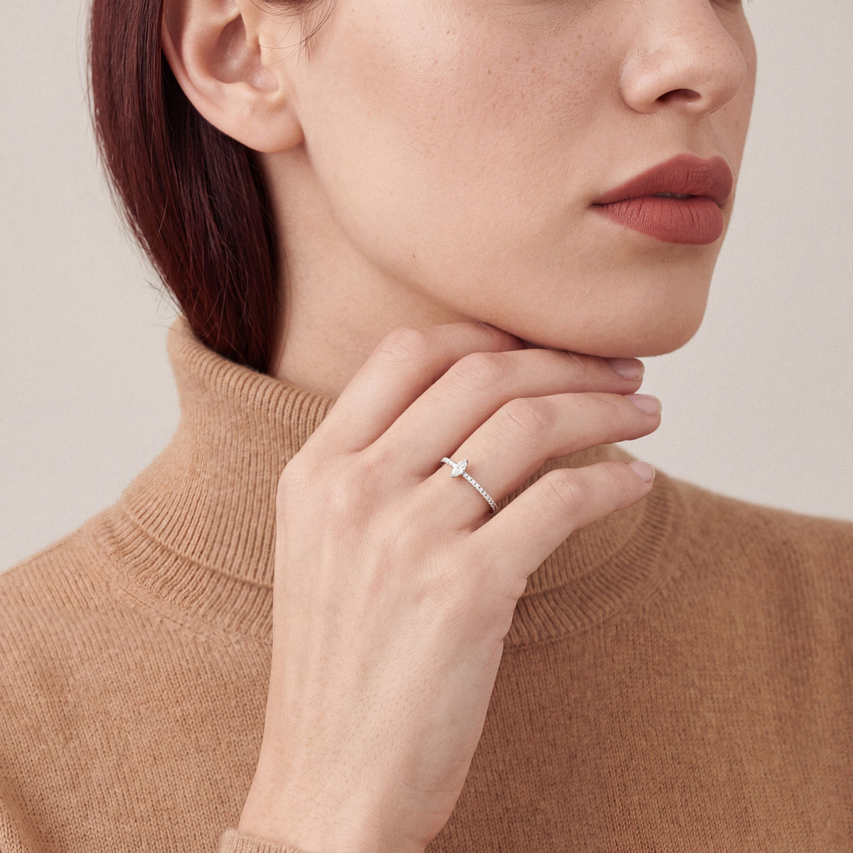 Woman in a camel turtleneck wearing a natural marquise diamond solitaire ring, hand along the jaw