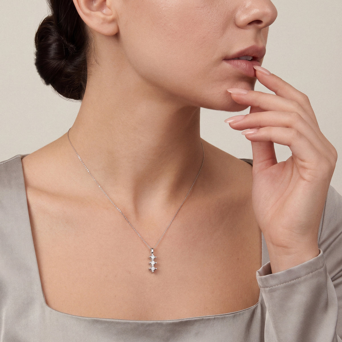 Woman in an oyster-grey satin top wearing the three-stone natural diamond star drop pendant necklace in 14K white gold