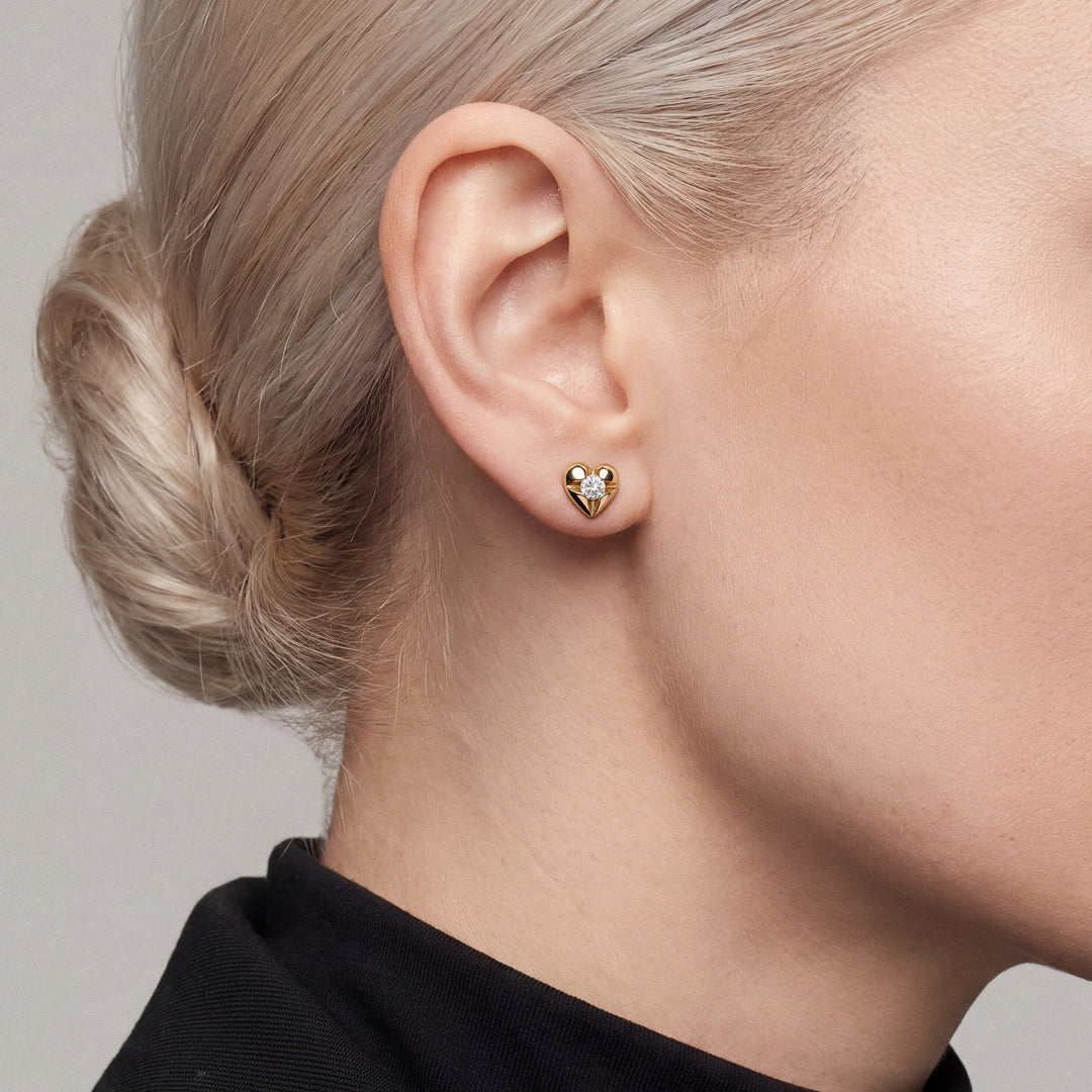 Woman in a black tuxedo jacket and high mock neck wearing a natural diamond heart stud earring in 14K yellow gold