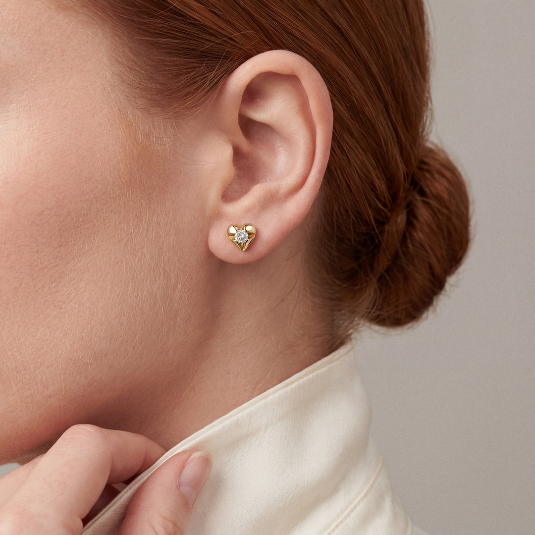 Woman in an ivory silk shirt with a turned-up collar wearing a natural diamond heart stud earring in 14K yellow gold