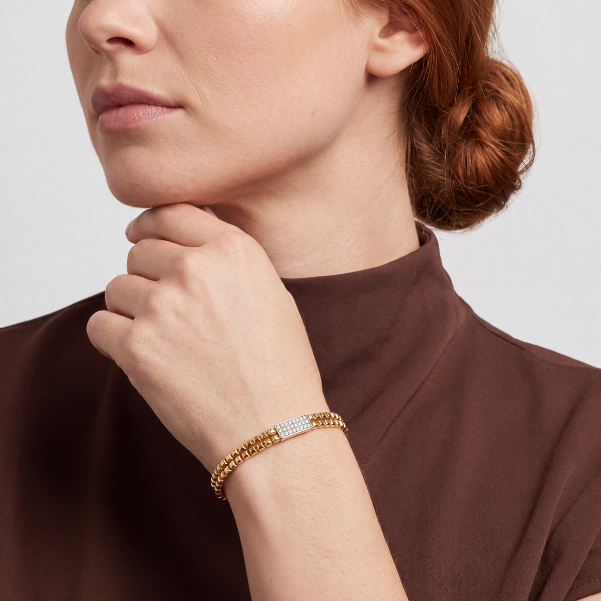Woman in a chocolate-brown silk mock-neck top wearing a natural diamond pavé bar hinged bangle in 14K yellow and white gold
