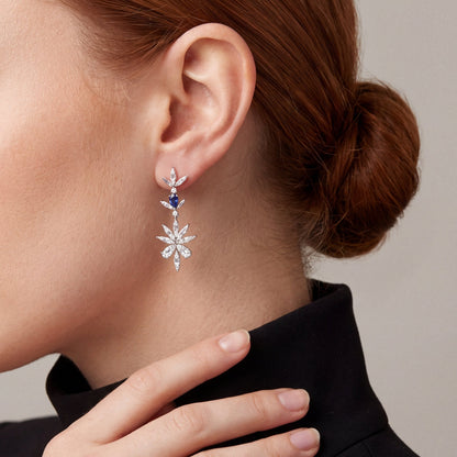 Model in a black blazer and high collar in profile, fingertips at her collar, wearing a natural diamond and sapphire flower drop earring in 14K white gold