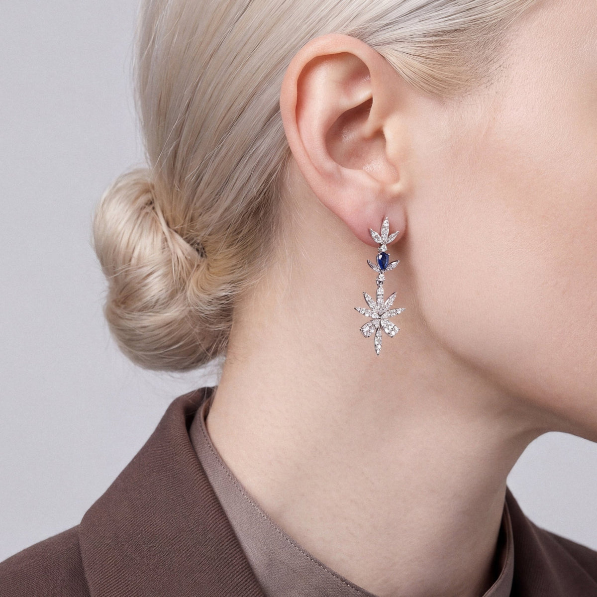 Model in a brown blazer and buttoned taupe shirt in profile wearing a natural diamond and sapphire flower drop earring in 14K white gold