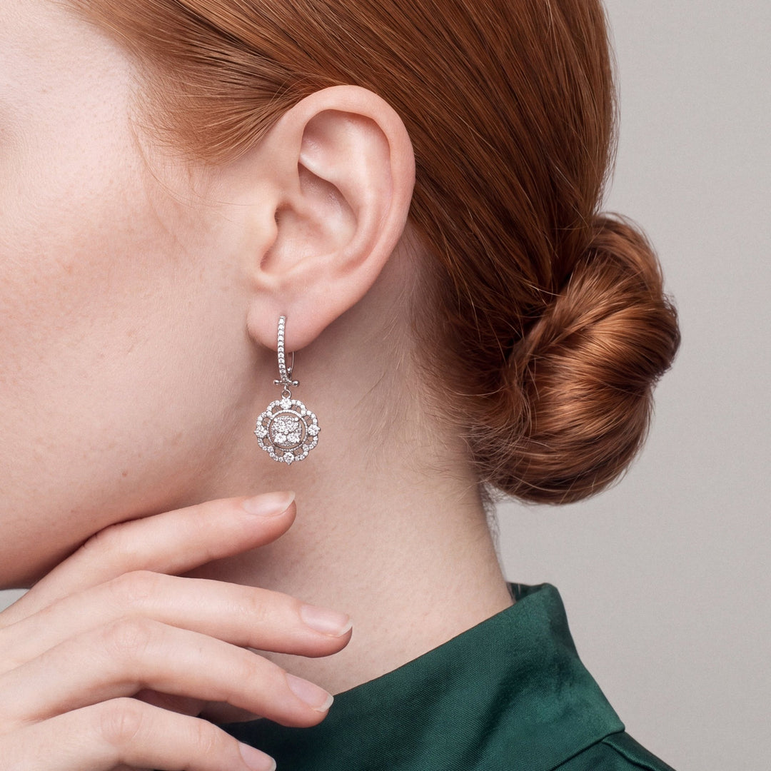 Woman in an emerald high-collar top, hand at her jaw, wearing a natural diamond flower halo drop earring in 14K solid white gold.