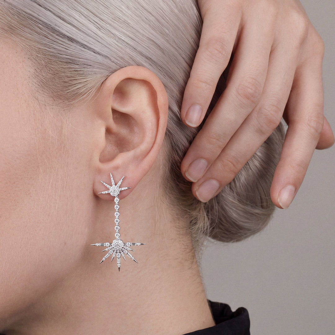Woman in a black mock-neck top with her hand in her hair, wearing a natural diamond starburst drop earring in 18K white gold