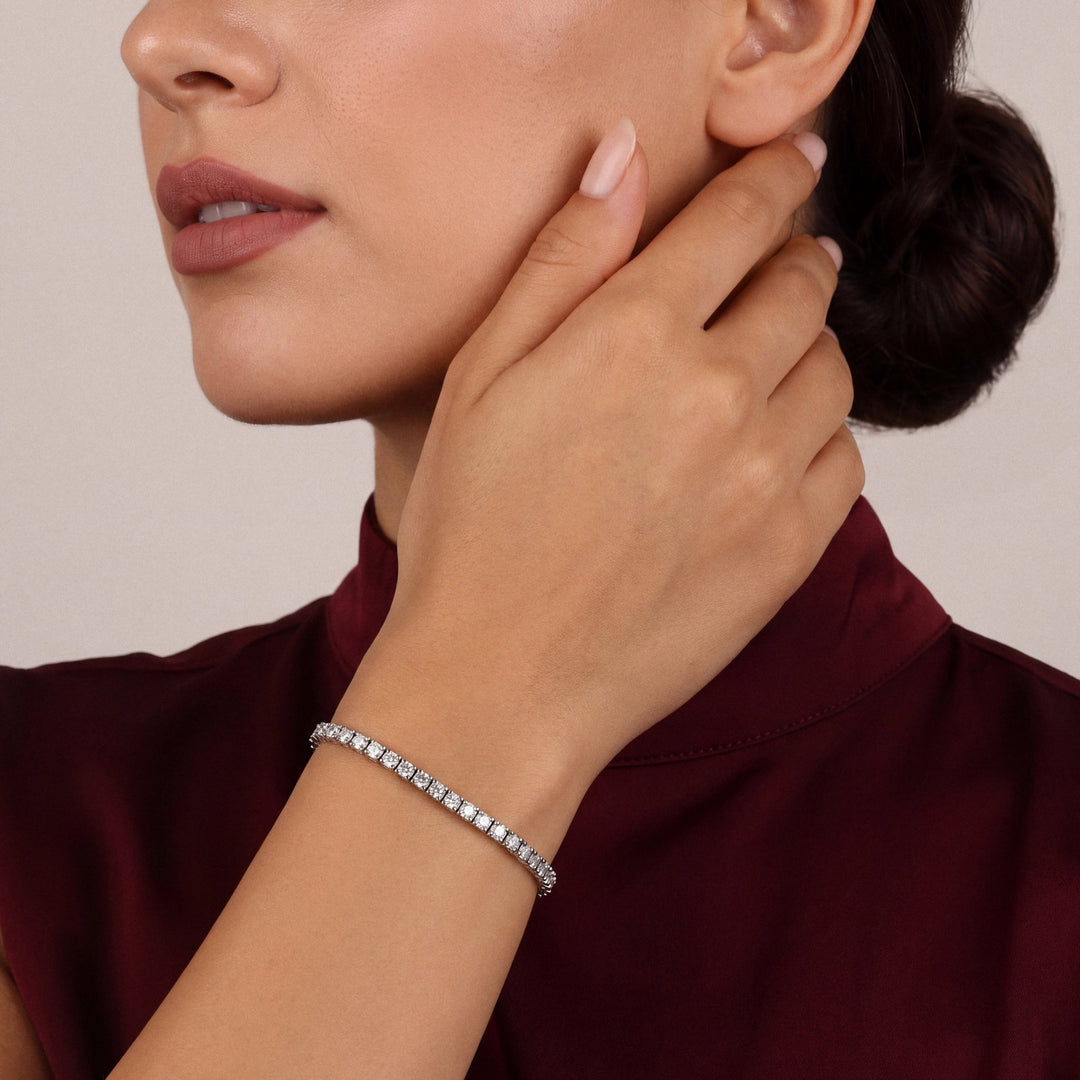 Woman in an oxblood mock-neck top, hand at her jaw, wearing a 4.78 ct tw natural diamond tennis bracelet in 14K white gold