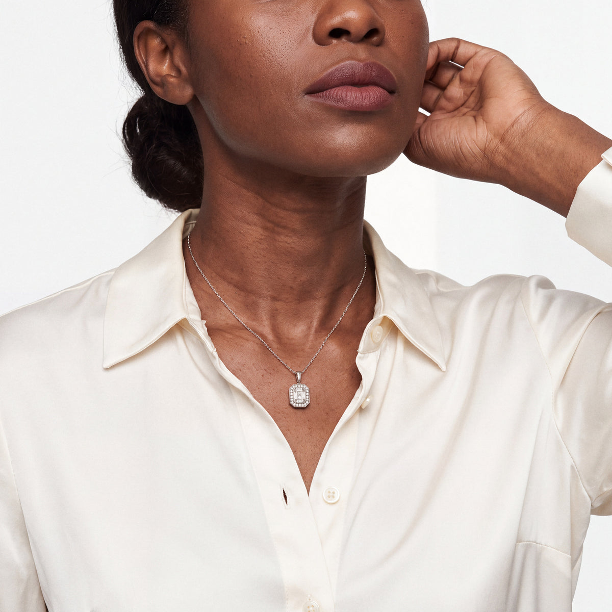 Model wearing the Art Deco baguette natural diamond halo necklace in 14K solid white gold with an ivory silk shirt