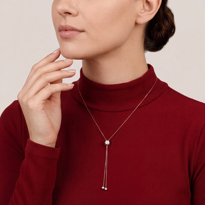 Woman in a claret-red crepe high-neck top wearing a baguette natural diamond lariat necklace with two diamond ball drops in 14K rose and white gold