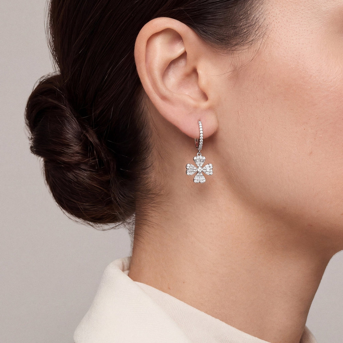 Woman in an ivory blazer with the collar turned up wearing a natural diamond clover drop huggie earring in 18K white gold, side profile