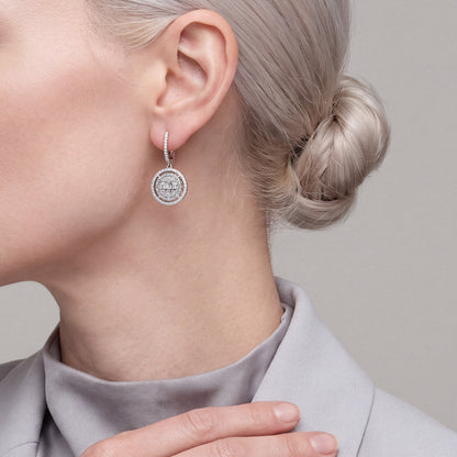 Woman in a dove-grey blazer wearing a 1.23 ct natural diamond baguette halo disc drop huggie earring in 14K white gold.