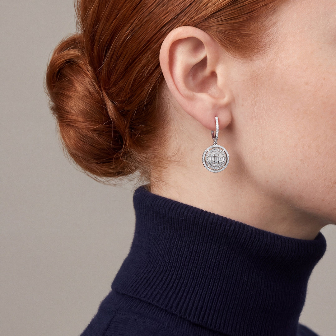 Woman in a navy turtleneck wearing a natural diamond baguette halo disc drop huggie earring in 14K solid white gold.