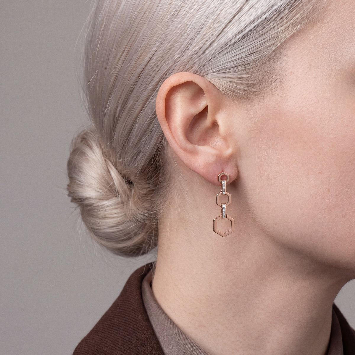 Model in a chocolate-brown blazer in profile wearing a baguette natural diamond hexagon drop earring in 14K rose gold