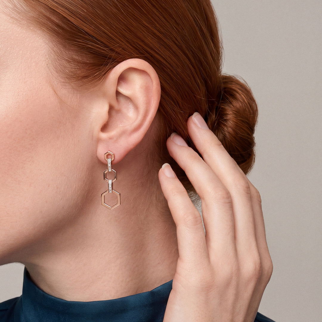 Model in a teal silk high-neck blouse with her hand in her hair, wearing a baguette natural diamond hexagon drop earring in 14K rose gold