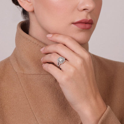 Woman in a camel cashmere funnel-neck coat wearing a 0.73 ct natural diamond baguette double halo ring in 14K white gold on the ring finger, fingers folded along the jaw
