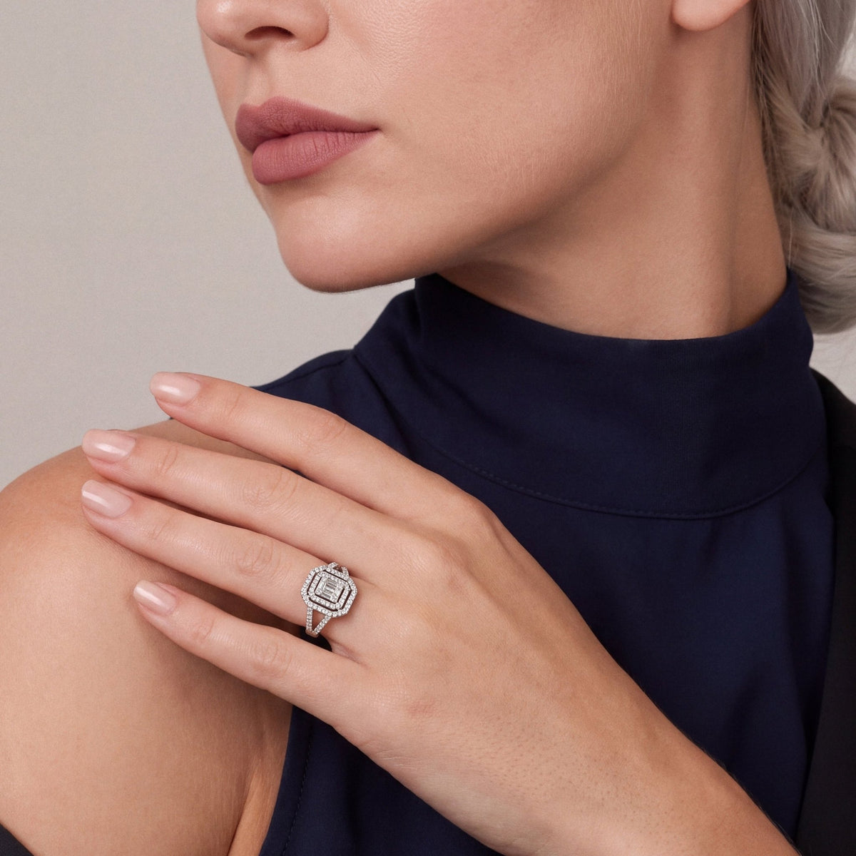 Woman in a navy high-neck top with a black tuxedo jacket slipped off the shoulder, wearing a 0.73 ct natural diamond baguette double halo ring in 14K white gold on the ring finger, hand on her shoulder