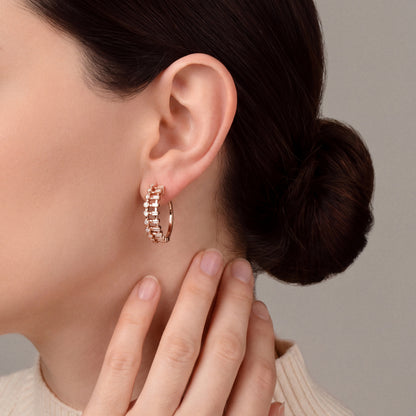 Model in a cream ribbed knit high neck with her fingertips at the side of her neck, wearing a baguette and round natural diamond ladder hoop earring in 14K rose gold