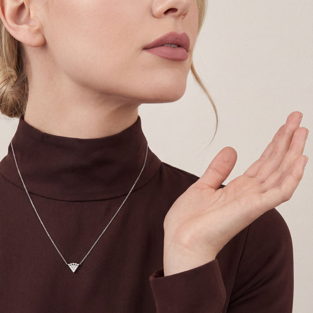 Woman in a chocolate-brown silk-crepe mock-neck top wearing a 0.12 ct natural diamond triangle necklace in 14K white gold.