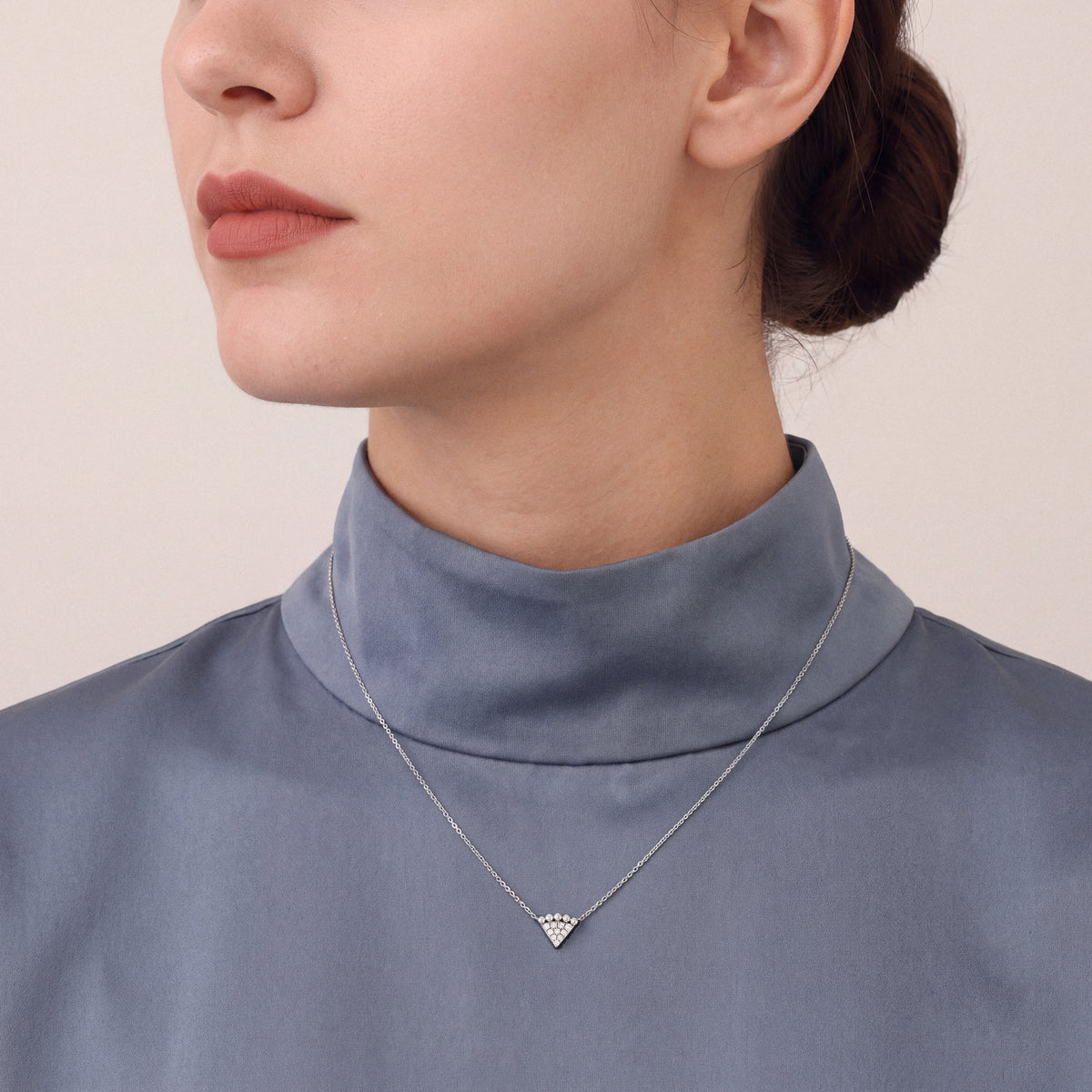 Woman in a slate-blue silk funnel-neck top wearing a beaded triangle natural diamond necklace in 14K white gold.