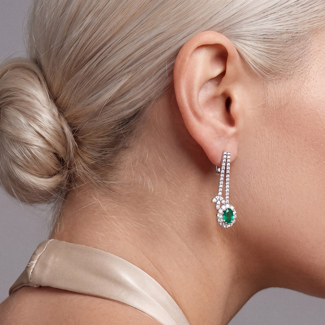 2.66 ct emerald and diamond drop earring in 18K white gold with a hinged lever-back, worn with a champagne silk halter