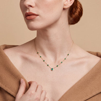Emerald and natural diamond halo station necklace in 14K yellow gold, worn with a camel cashmere coat off the shoulders
