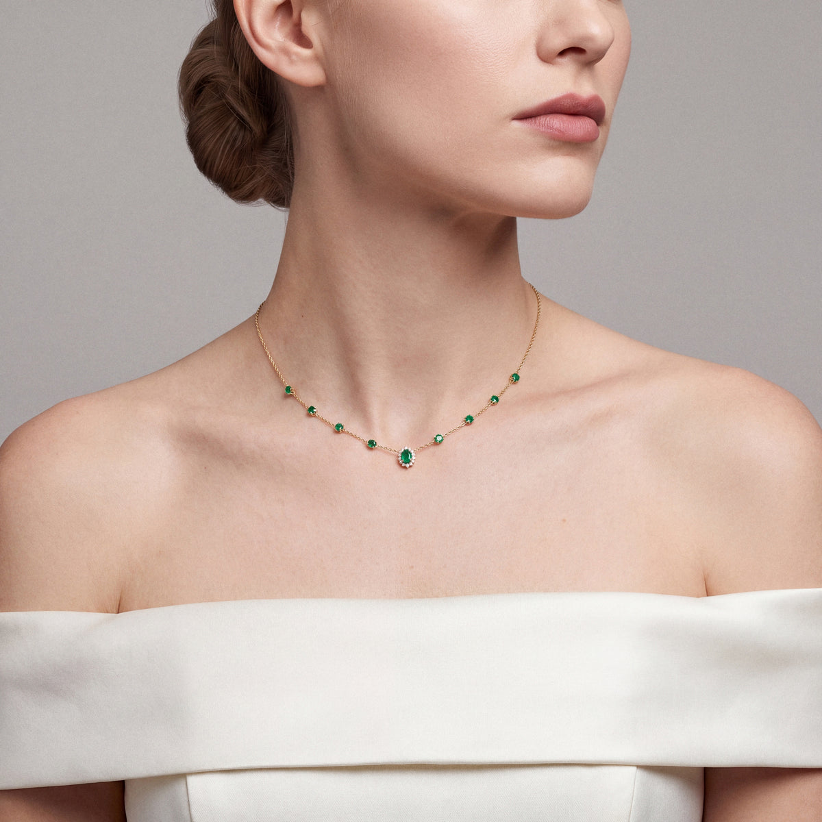 Eight emerald stations and an oval emerald diamond halo in 14K yellow gold, worn with an ivory off-shoulder satin gown