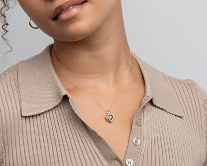 The 14K solid gold evil eye heart necklace worn with a collared knit top.