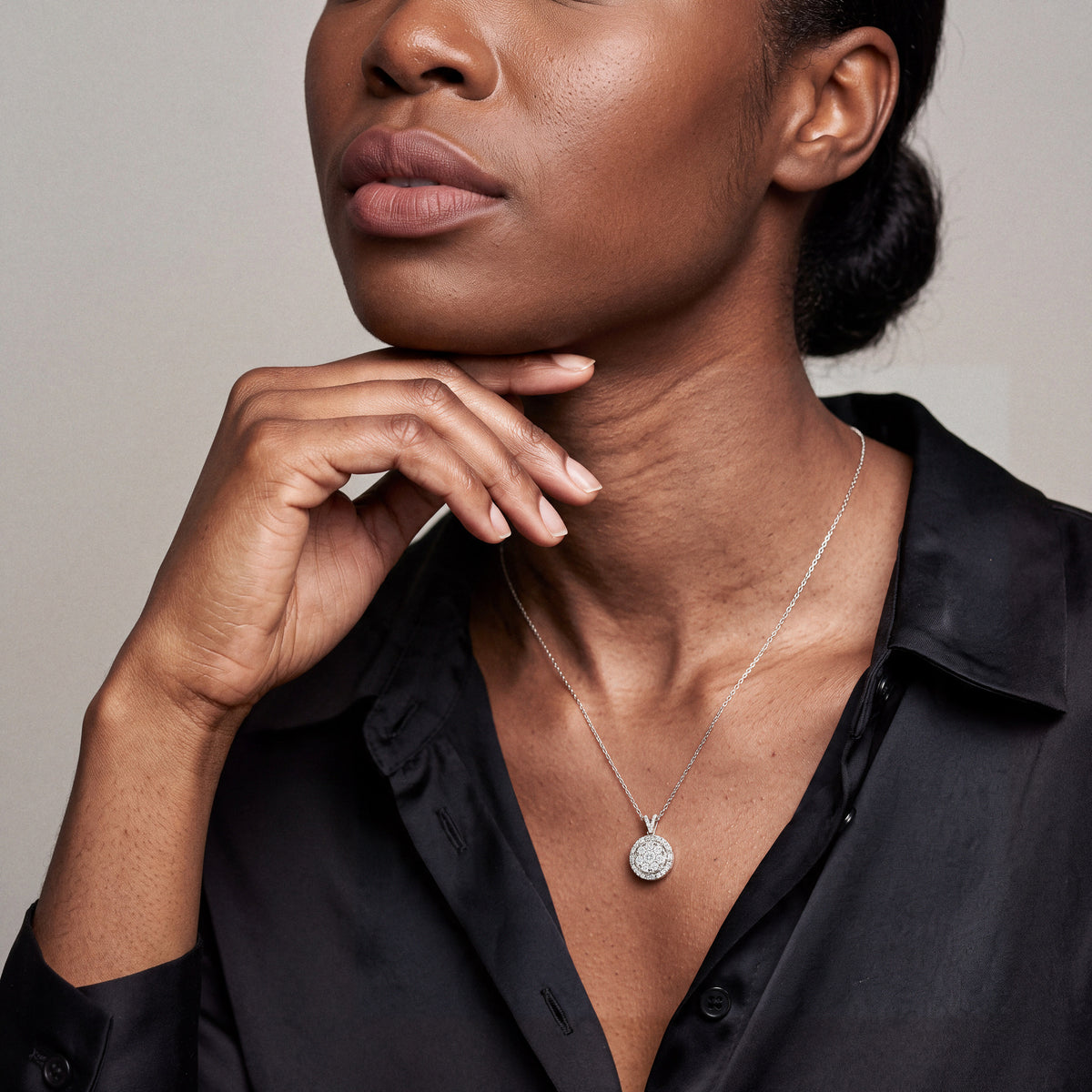 Model wearing the round diamond cluster halo pendant necklace in 14K white gold with a black silk blouse