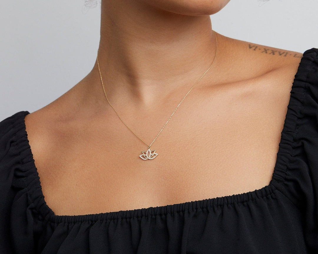 Close-up of the 14K solid gold lotus pendant worn above a black square neckline.