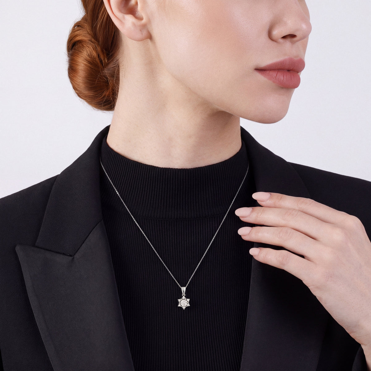 Woman in a black tuxedo jacket over a black mock-neck top wearing a natural diamond lotus star pendant necklace in 14K white gold.