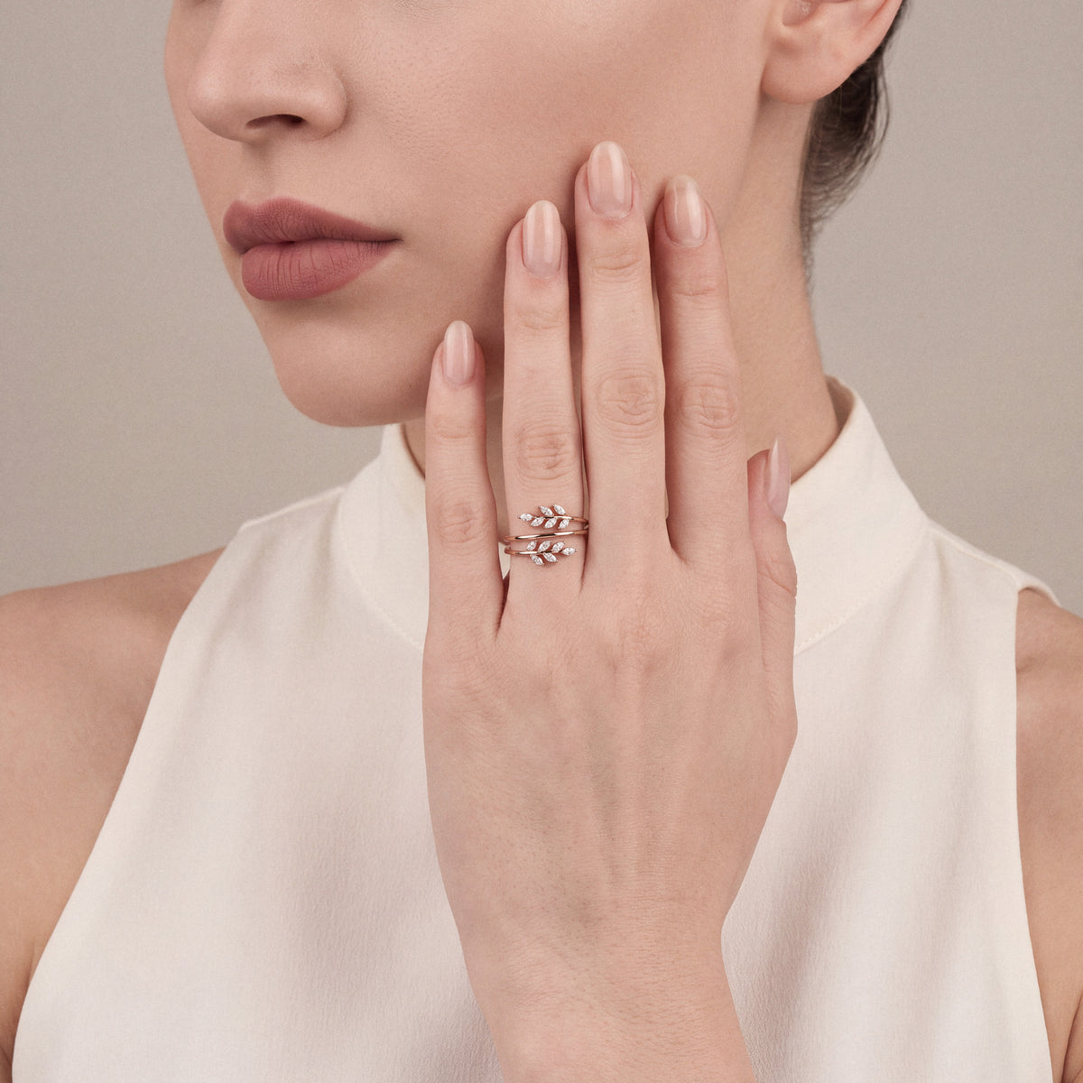 Woman in an ivory high-collar top wearing a marquise natural diamond leaf wrap ring in 14K rose gold on the ring finger, palm resting on her cheek