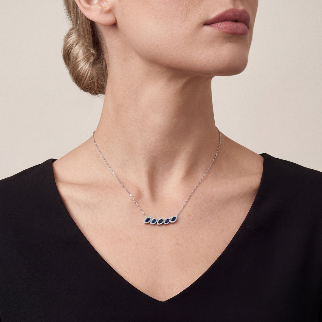 Woman in a black V-neck top wearing the marquise natural sapphire and natural diamond halo necklace in 14K white gold