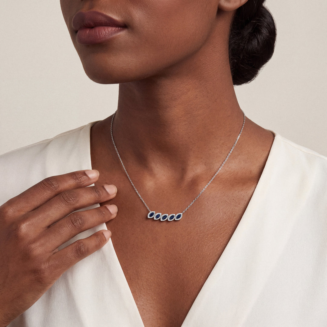 Woman in an ivory silk blouse wearing the marquise natural sapphire and natural diamond halo necklace in 14K white gold