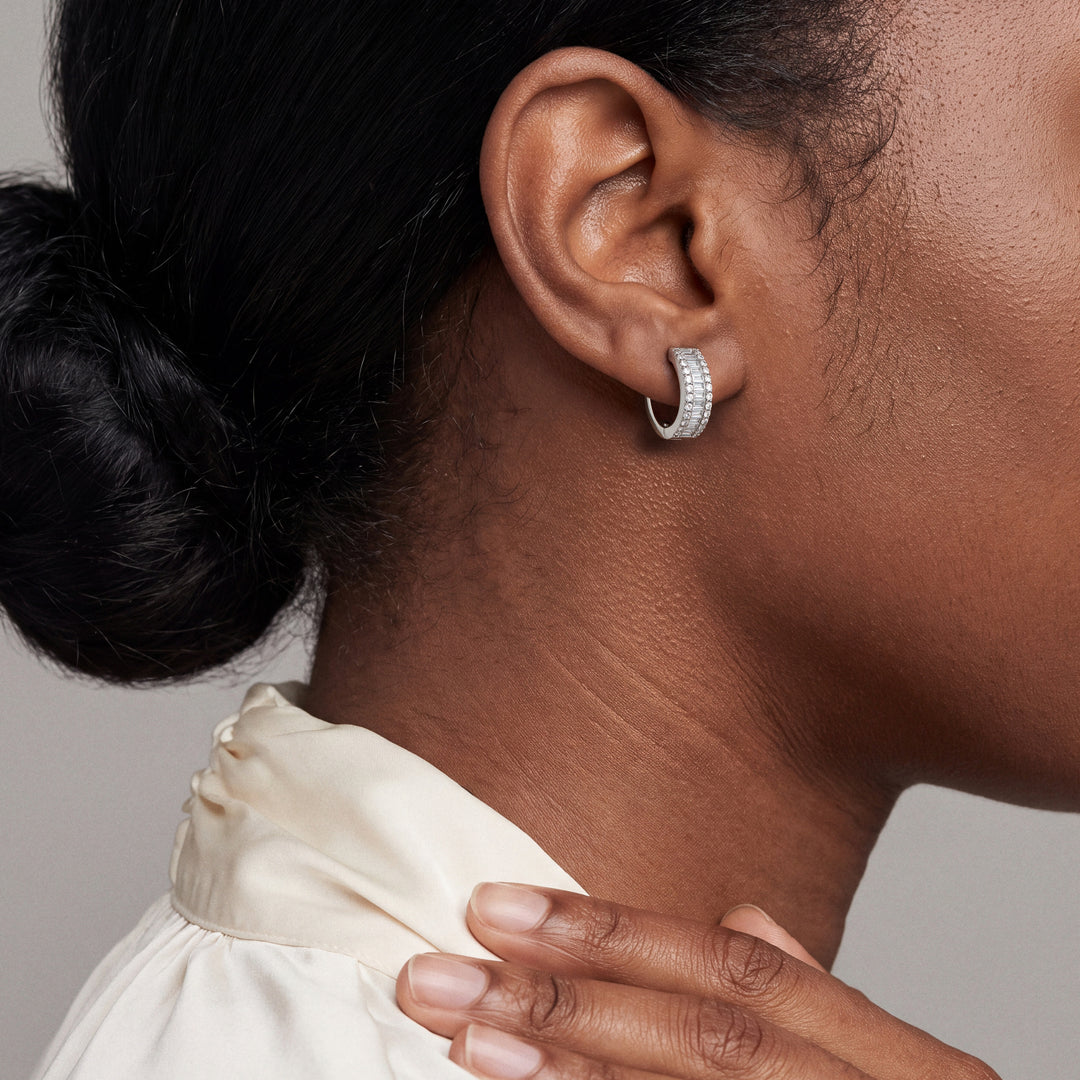 Model wearing the baguette and pave diamond huggie hoop earring, hand resting at the collar