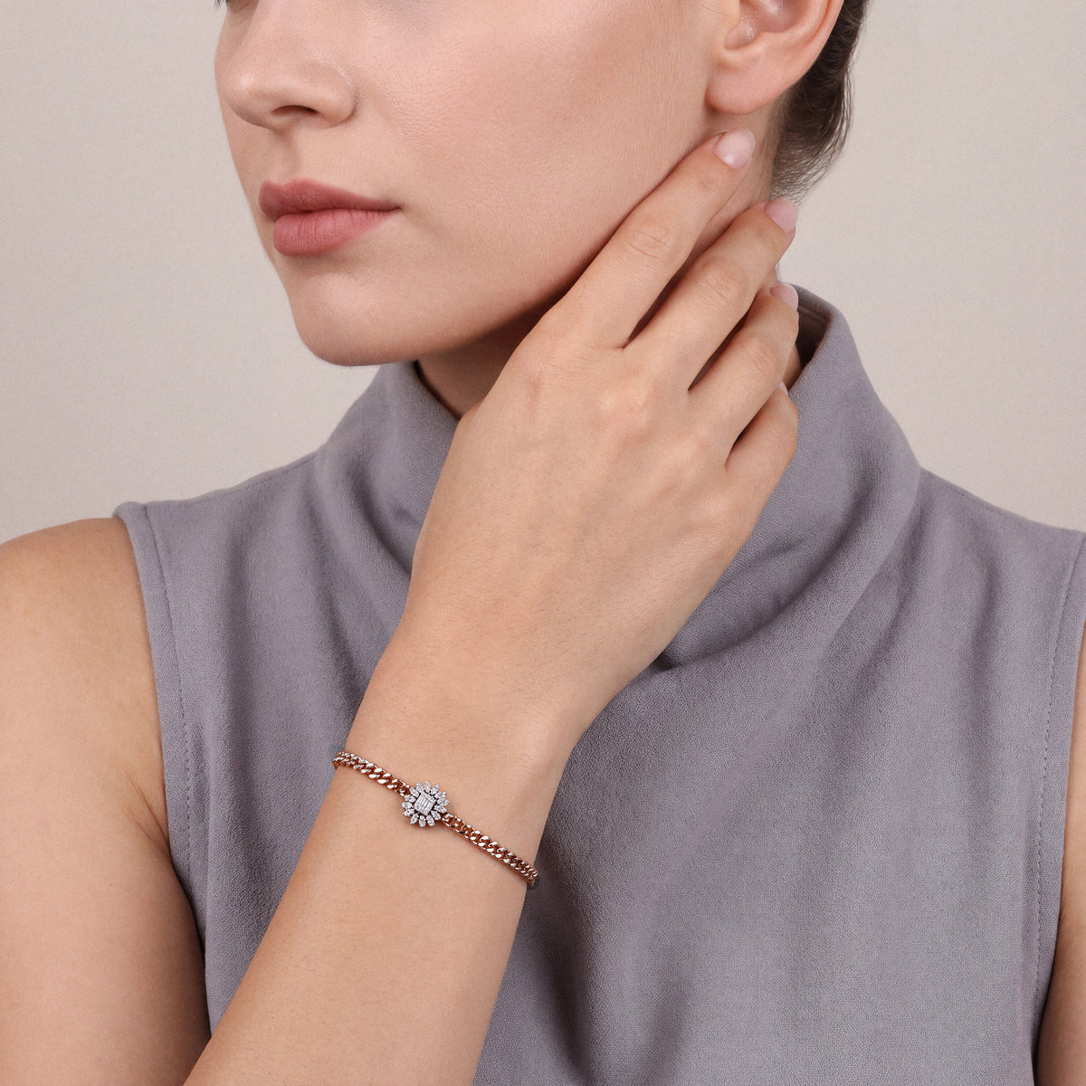 Woman in a dove-grey cowl-neck top wearing a natural diamond sunburst rose gold curb bracelet, fingertips at the jaw
