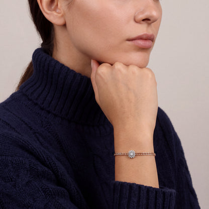 Woman in a navy cable-knit turtleneck wearing a natural diamond sunburst rose gold curb bracelet, fist under the chin