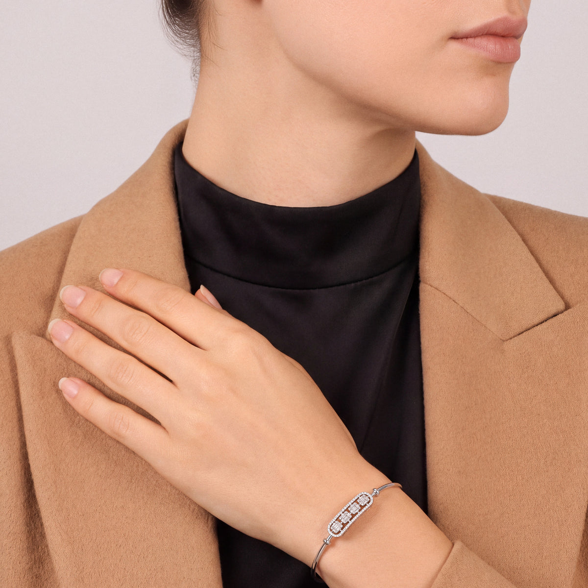 Woman in a camel blazer and black high-neck top wearing a natural diamond baguette bar bangle in 18K white gold