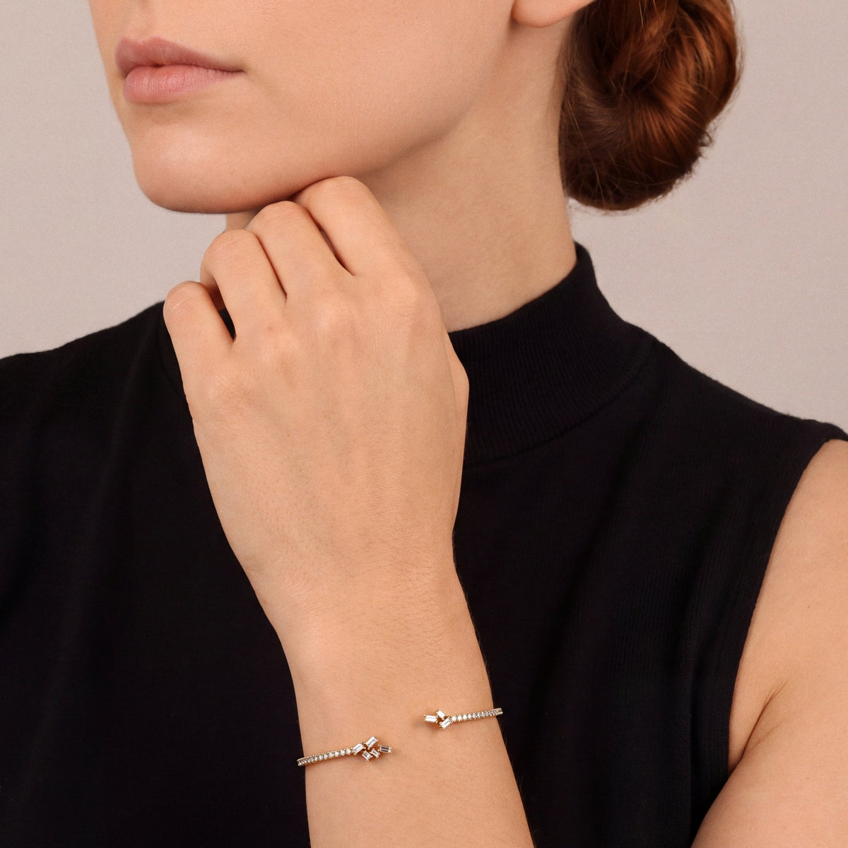 Woman in a black high-neck top wearing a natural diamond baguette cluster open cuff bracelet in 18K yellow gold