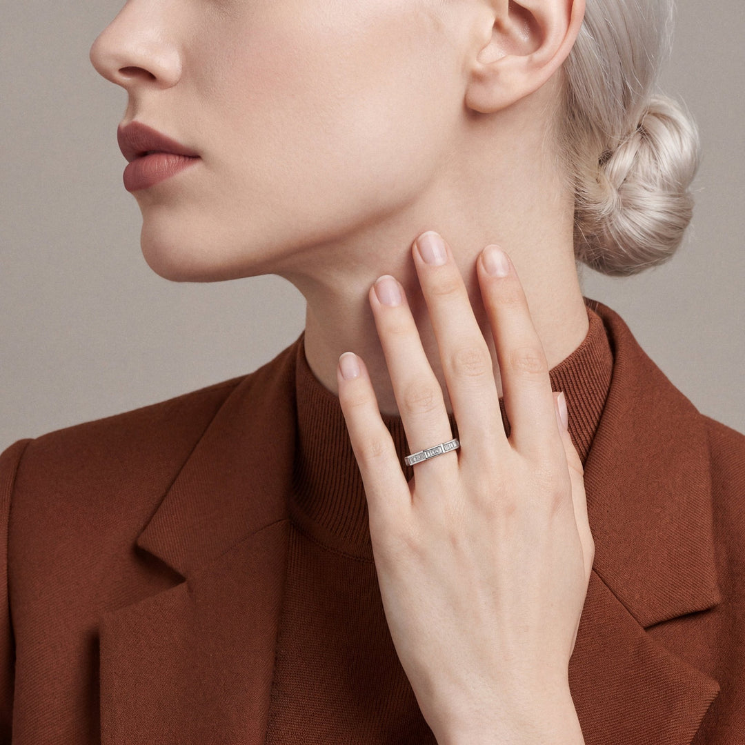 Woman in a rust blazer wearing a baguette diamond eternity ring in 14K white gold, fingertips at the neck