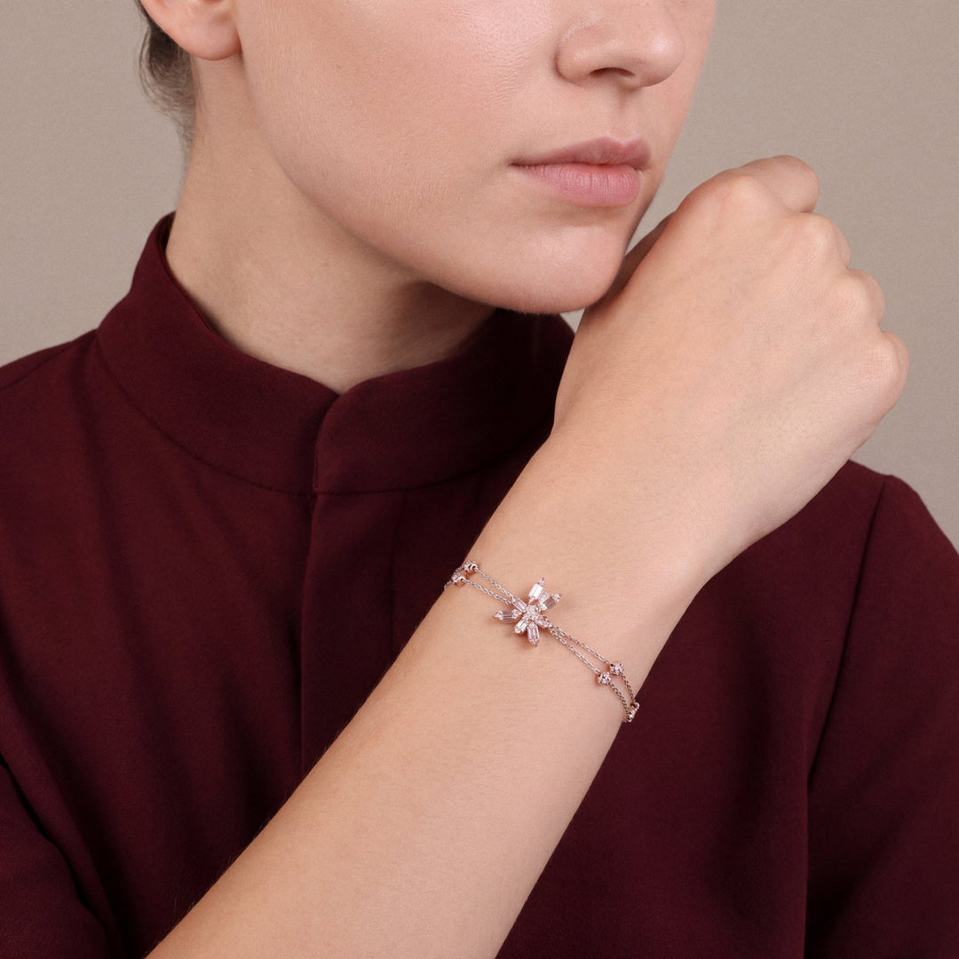 Woman in an oxblood stand-collar top wearing a natural diamond baguette flower double chain bracelet in 14K rose and white gold, fist resting at the jaw