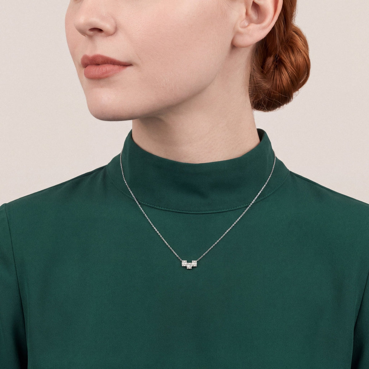 Woman in an emerald funnel-collar top wearing a natural diamond baguette geometric bar necklace in 18K white gold