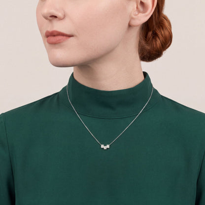 Woman in an emerald funnel-collar top wearing a natural diamond baguette geometric bar necklace in 18K white gold